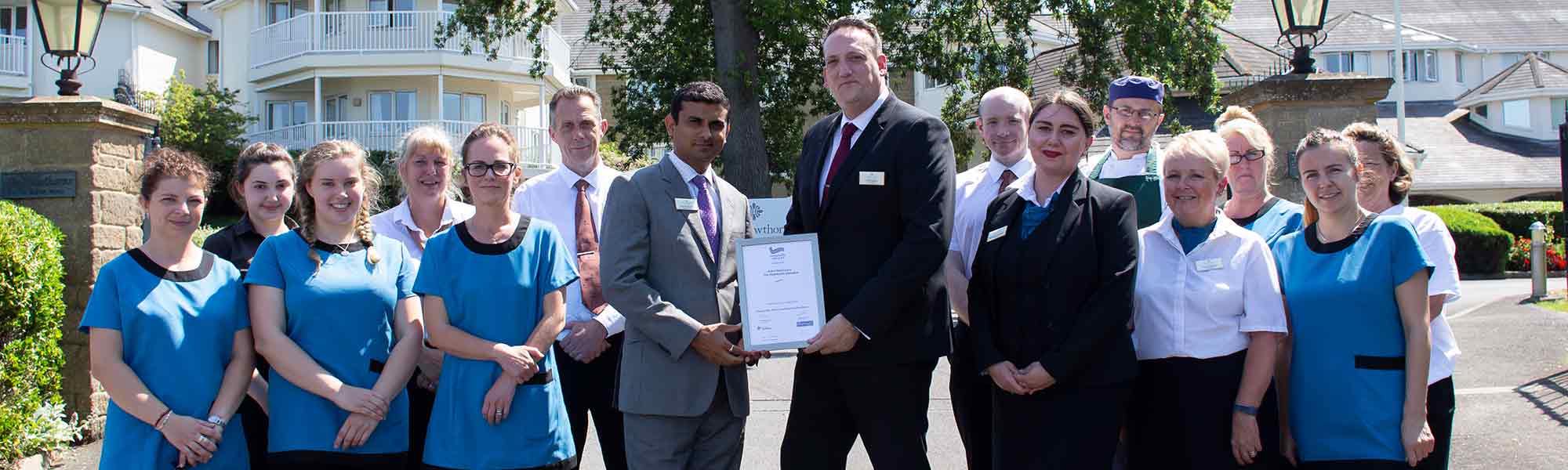 Davesh Kumar and Hawthorns Clevedon staff with Hospitality Assured Award banner hero